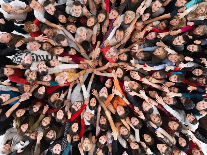 High angle view of large group of happy people joining hands in unity and looking at camera.