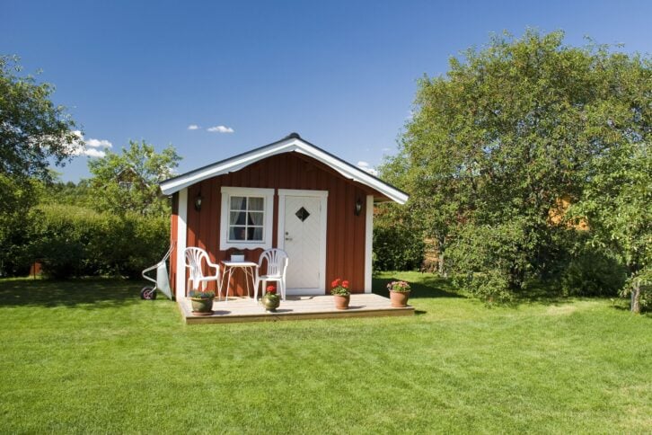red tiny house with porch in an idyllic area with cherry trees in the background