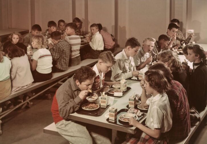 A group of schoolchildren sitting at tables as they eat their lunch in the school lunchroom, United States, circa 1965.