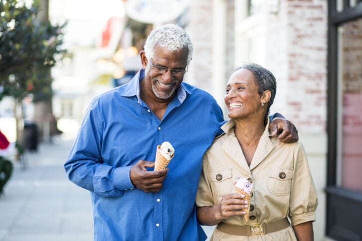 Senior couple eating ice cream walking down the street of quaint downtown area, shops in the background