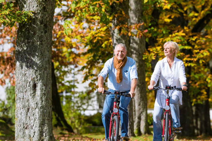 Senior man and woman couple on bicycles enjoying changing leaf colors during autumn in a park with lots of trees, selective focus, trees with beginning yellow and orange leaves