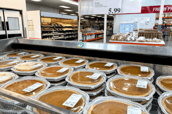 Several rows of Kirkland pumpkin pie for sale at a Costco in an outside refrigerator in the foreground, two baked good in the background