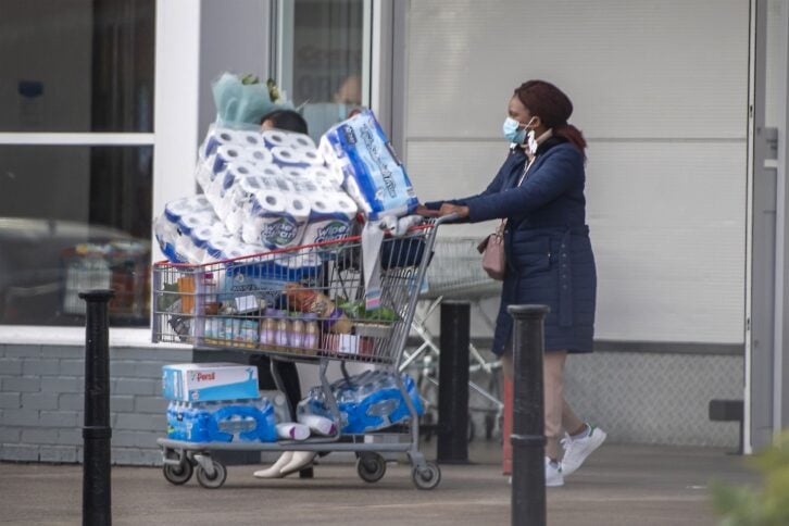 Shoppers leave a Costco store in Trafford on December 22, 2020 in Manchester, England, in front area one woman has a cart filled with many items including paper towels