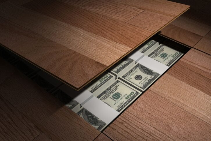 Private stash of stacks of U.S. $100 dollar bills hidden under the floor boards, a sliver is revealed, flooring opened, shadowing