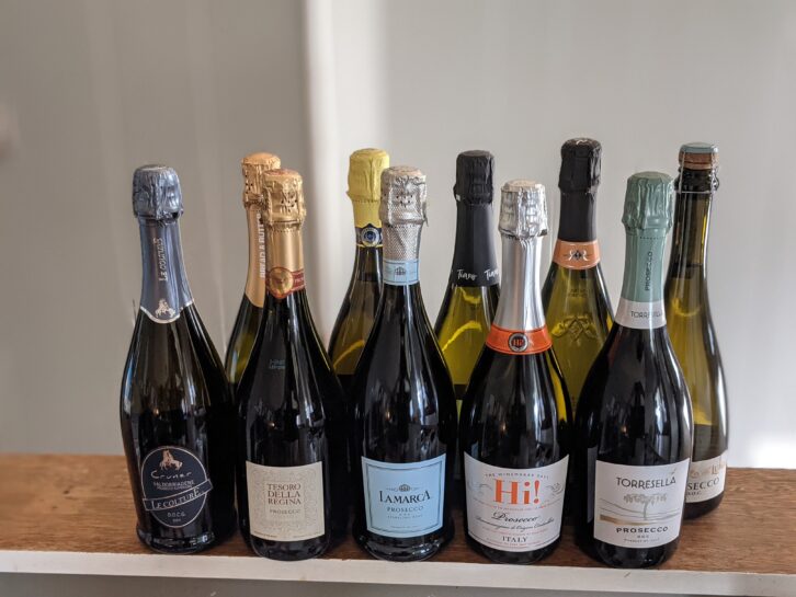 Ten sealed bottles of Proseccos on a wooden ledge, white panel wooden wall blurred in the background