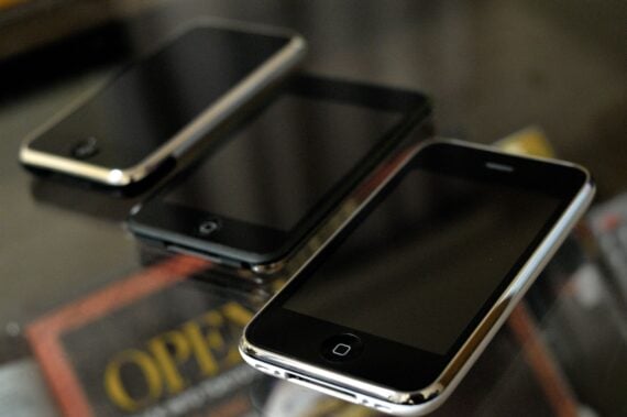 The Original iPhone, iPod Touch, and iPhone 3G on a glass table with magazines underneath
