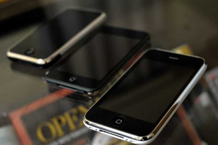 The Original iPhone, iPod Touch, and iPhone 3G on a glass table with magazines underneath