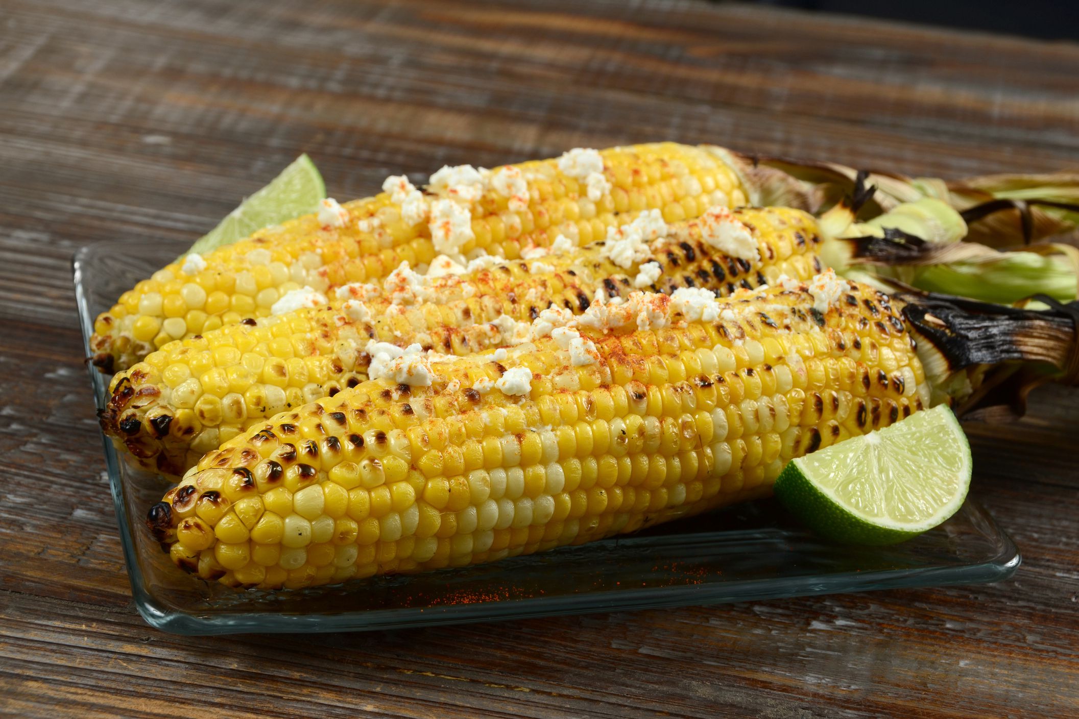 Three pieces of elote mexican grilled corn on a glass plate on a wooden table