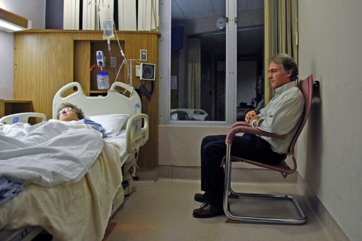 Man sitting in a chair next to a woman in a hospital bed