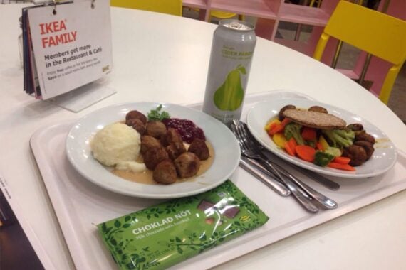 Two Swedish meatball meals on plates with utensils and soda can on table with yellow chairs at Ikea Restaurant