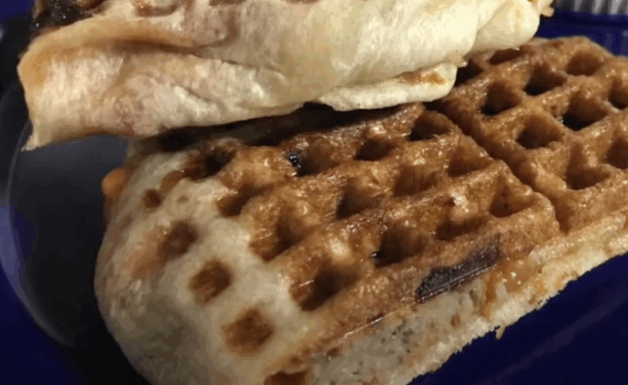Two folded burritos with grill marks are stacked on a dark blue plate. The golden brown tortillas appear crispy, with a waffle-like texture from being pressed in a waffle iron.