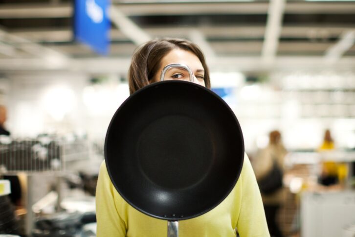 Woman peeking through loop of skillet while looking at the camera with a blurred background of the inside of a store
