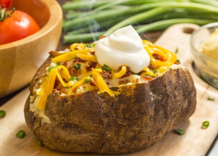 Baked potato with chives, black pepper and sour cream on a white plate.