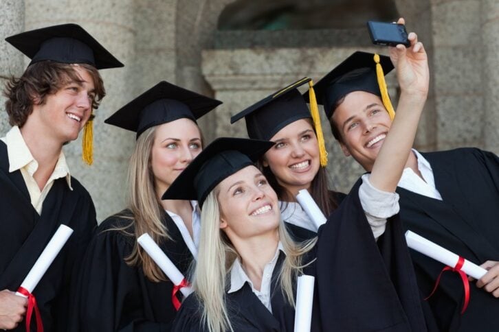 group of students in graduation gowns smiling and posing for a group selfie