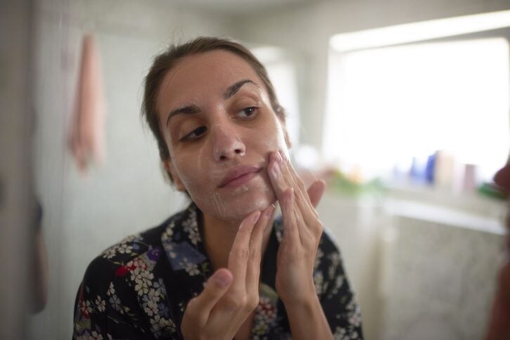 woman in bathroom putting on acne treatment