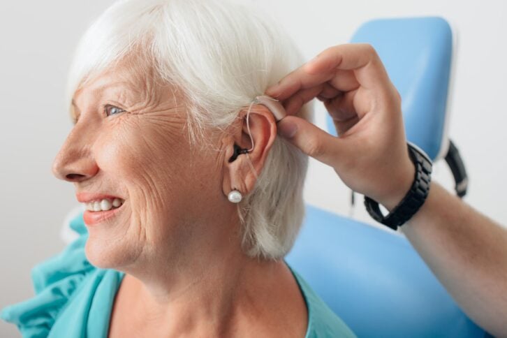 senior woman getting hearing aid adjusted at doctor office