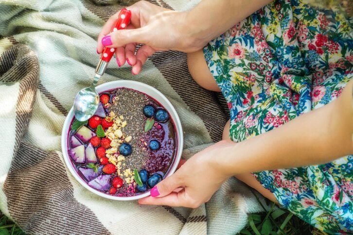 acai bowl with chia seeds and berries over blanket, held by two hands with nail polish