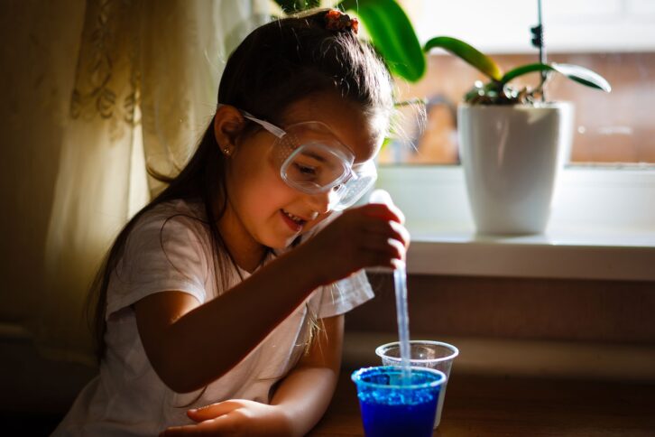 little girl experimenting in elementary science class with protective gloves and glasses