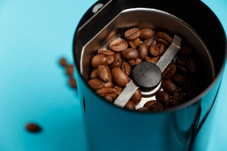 electric coffee grinder with roasted coffee beans on the kitchen table with blue tabletop