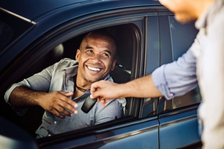 man in driver's seat receiving keys to rental car