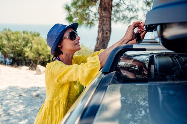woman opening cargo box on roof rack at beach