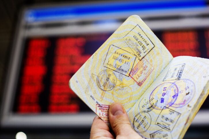 Passport with custom entry stamps in-front of information board at airport