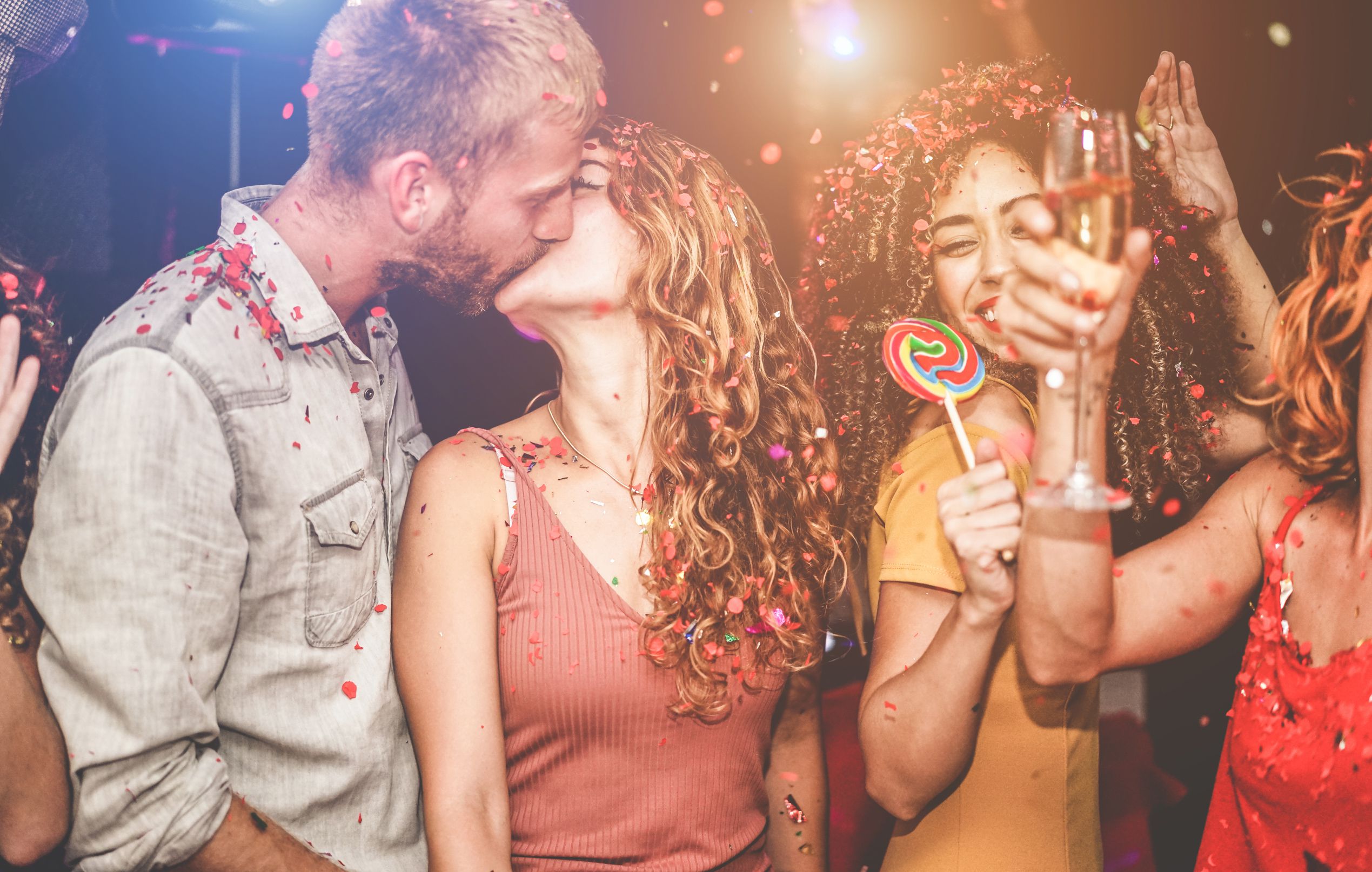 Trendy happy friends dancing at vintage night party with confetti, champagne and candy lollipop - Young people having fun inside nightclub - Youth and nightlife concept - Focus on girls faces