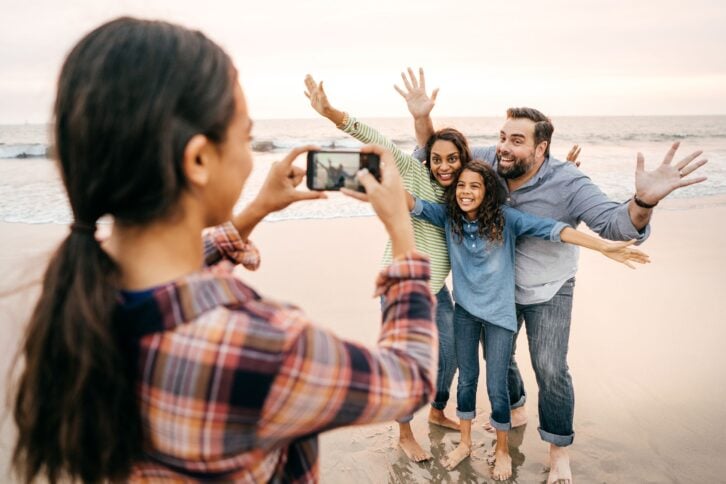 daughter taking photos of her parents and sister on the beach
