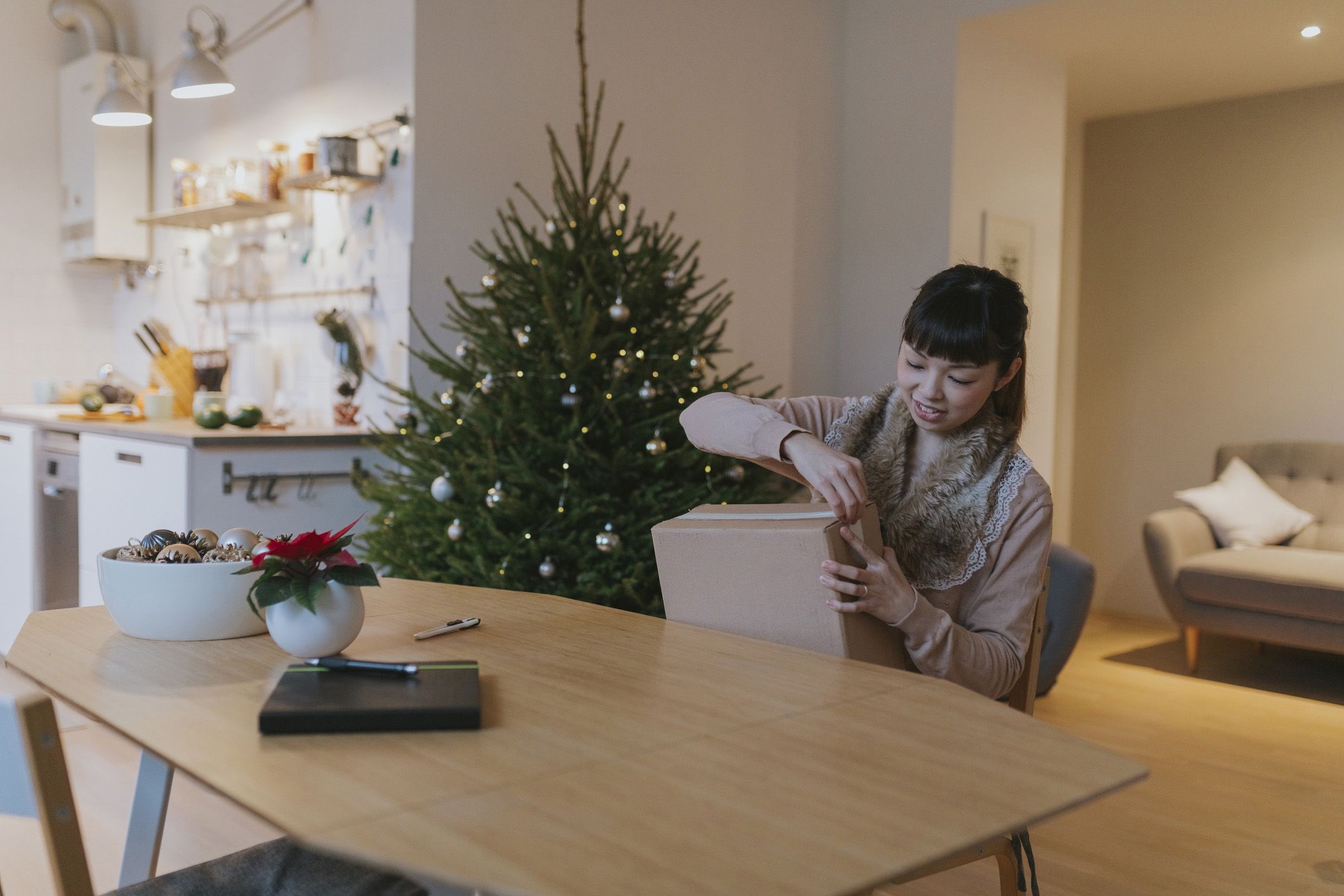 woman opening box; christmas tree in background