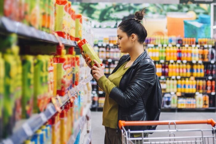 woman reading nutrition label of juice at grocery store