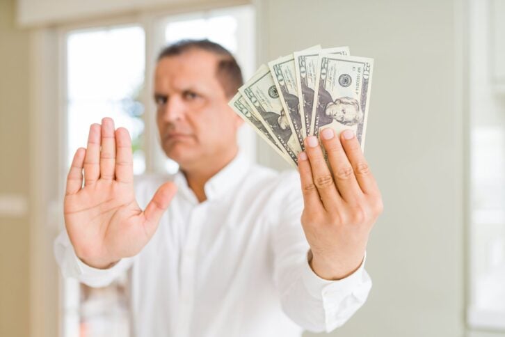 Middle age man holding bunch of dollars with open hand doing stop sign with serious and confident expression, defense gesture
