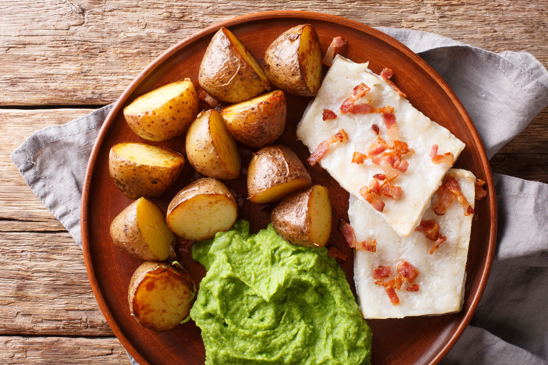 Norwegian cod lutefisk served with pea puree, potatoes and bacon close-up on a plate. Horizontal top view from above