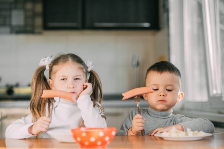 Boy and girl children in the kitchen eating sausages with pasta is very fun and friendly very sweet