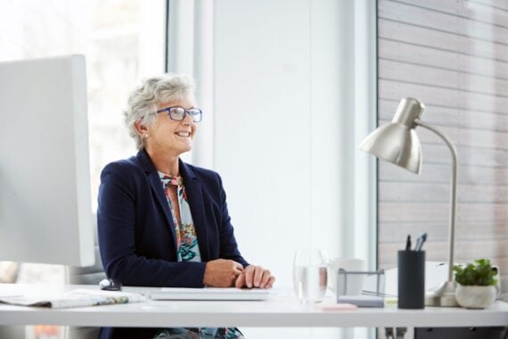 senior woman looking into distance and smiling sitting at desk in office