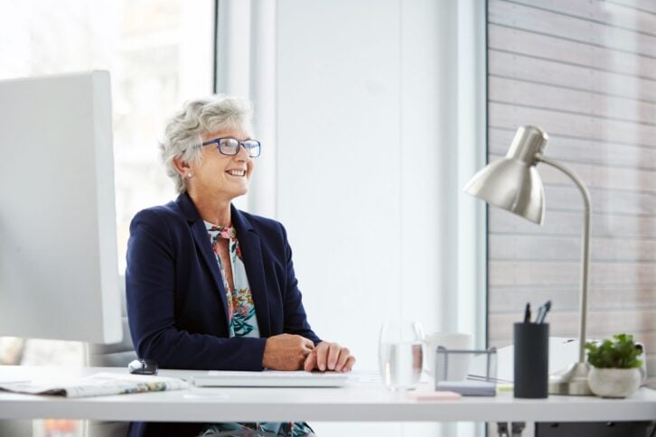 senior woman looking into distance and smiling sitting at desk in office