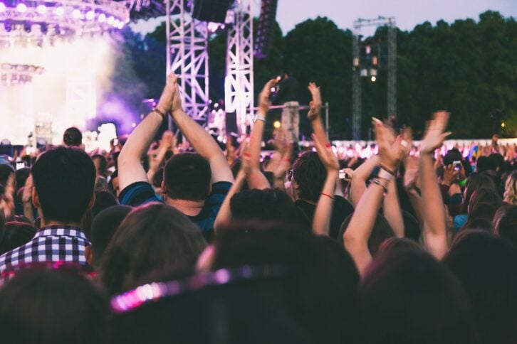A big concert crowd having fun in front of the stage. The audience is dancing and applauding rhythmically to the music.