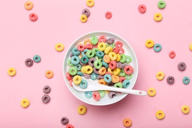 Colorful corn rings in bowl with milk and spoon on pink background
