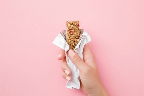 young woman hand holding cereal bar on pastel pink table
