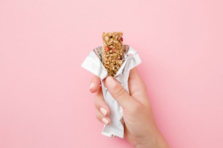 young woman hand holding cereal bar on pastel pink table