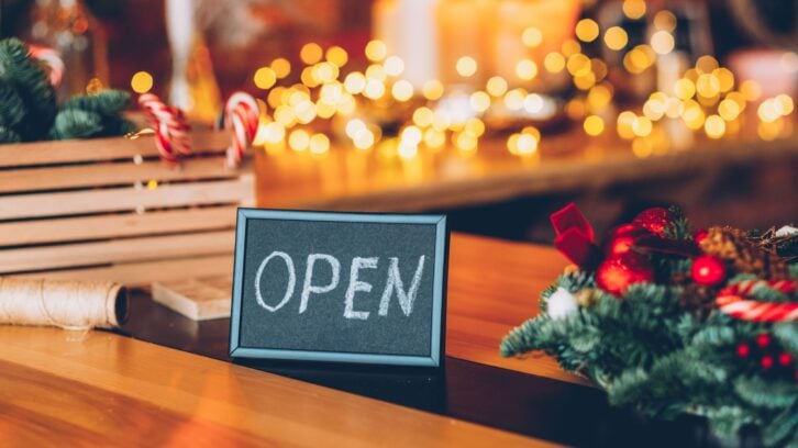 Florist workshop. Christmas decor. Welcoming sign. Frame with open lettering over blur festive interior.