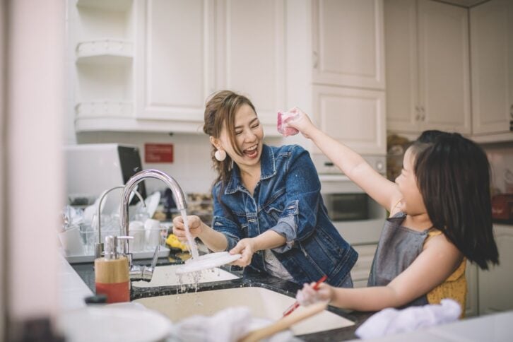an asian chinese mother washing dishes with her daughter in the kitchen and having fun time bonding