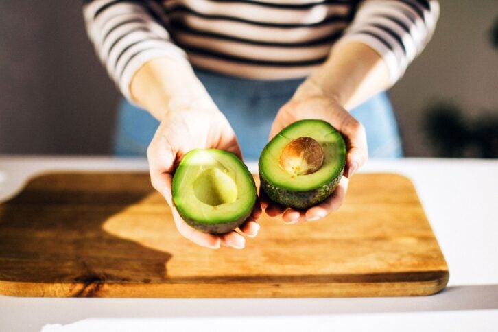 Unrecognizable woman holding in her hands opened avocado, close up