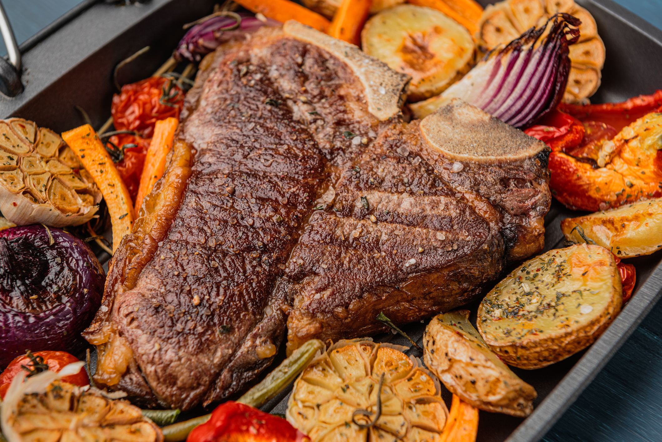 tender and juicy steak on the bone grilled next to baked and grilled vegetables, the concept of tasty and healthy nutrition