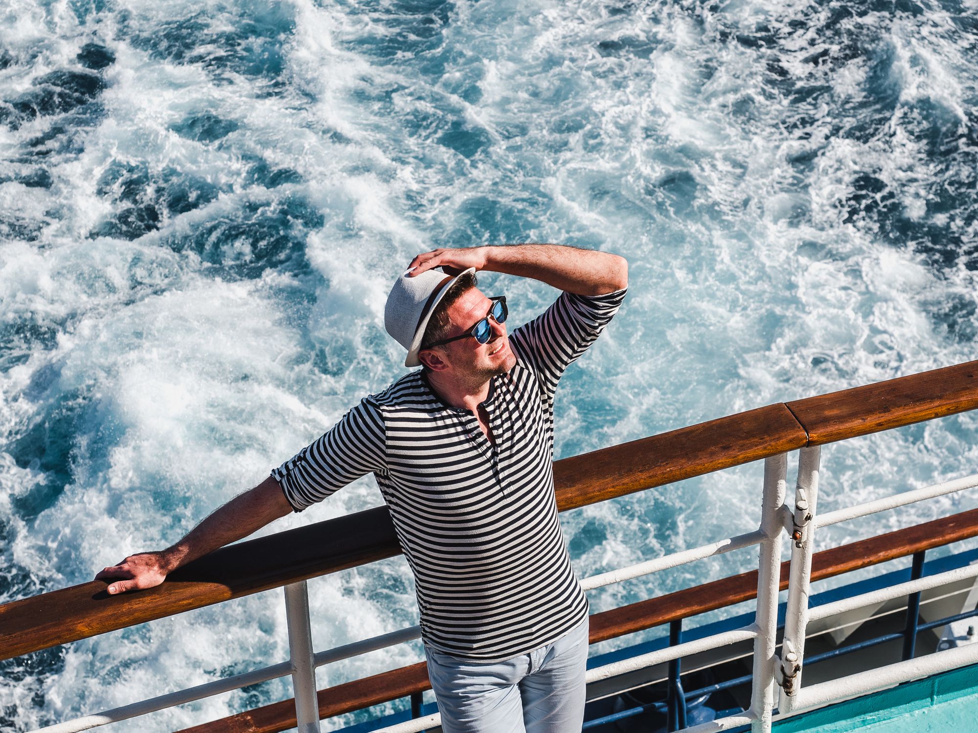 Smiling man on the empty deck of a cruise liner on the background of sea waves. Top view, close-up. Concept of leisure and travel