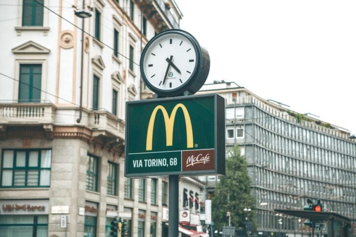 Italy, Milan, May 30, 2019: A street clock and a McCafe sign on the background of urban buildings and houses.
