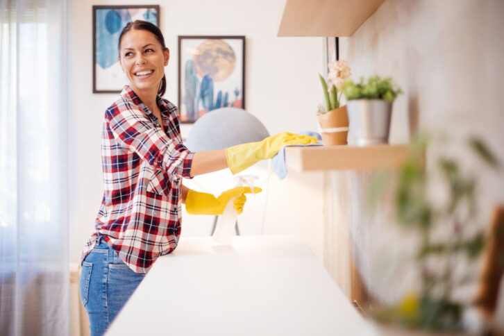 Beautiful Caucasian  young woman in casual clothes with yellow gloves cleaning furniture in living room at home.