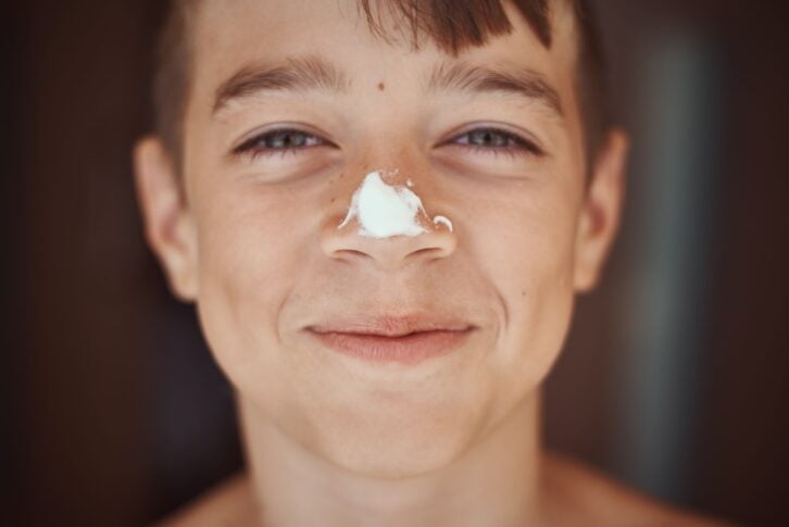 Happy smile boy with sunscreen cream on nose, close up portrait. Summer holidays and vacation concept
