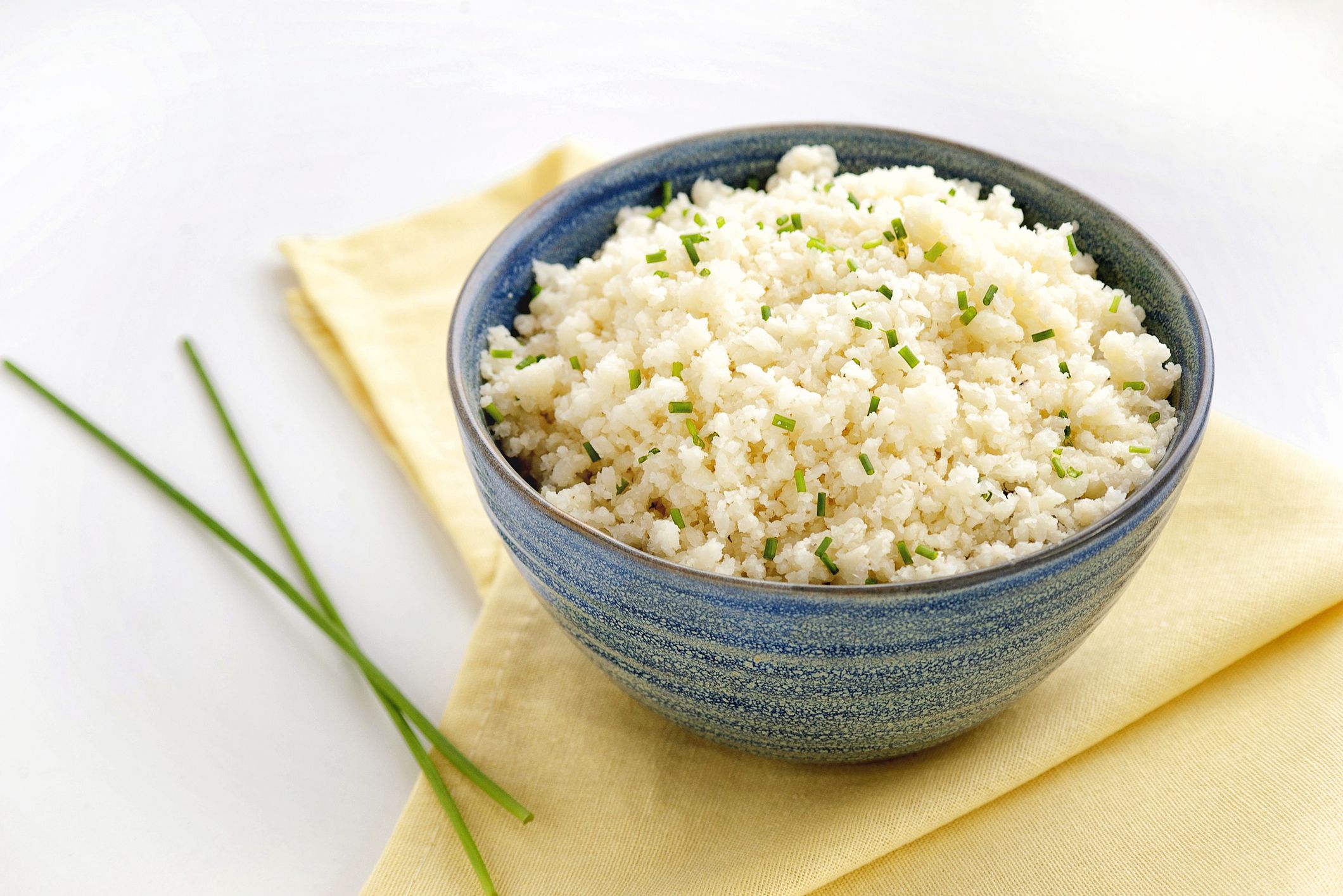 Cauliflower rice. Ketogenic and paleo food. Large portion in a blue bowl on a yellow napkin. Close up and horizontal orientation. Copy space.