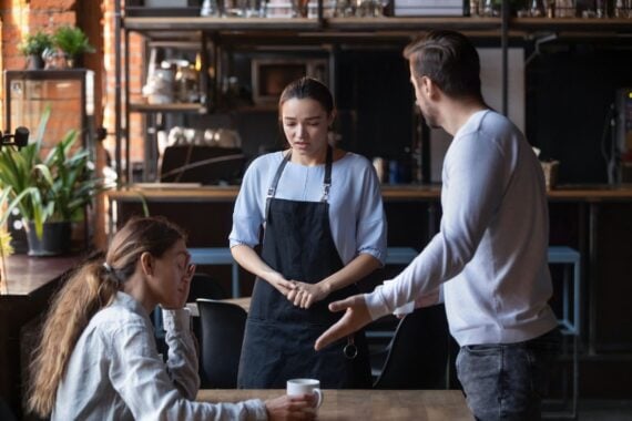 Furious man stand dispute with guilty waitress bringing wrong order, mad client couple get nervous disappointed with bad service or waiter incompetence, blame stuff yell and shout in public place