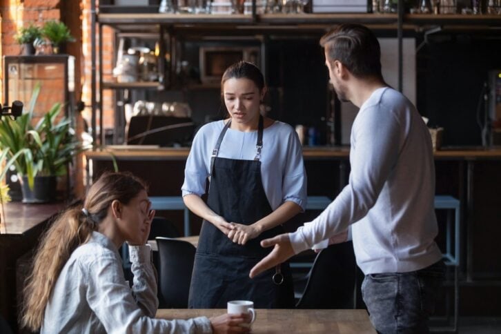 Furious man stand dispute with guilty waitress bringing wrong order, mad client couple get nervous disappointed with bad service or waiter incompetence, blame stuff yell and shout in public place